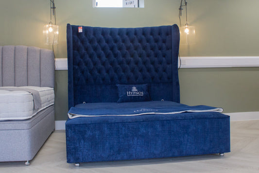 Blue tufted bed with Hypnos logo in a room setting