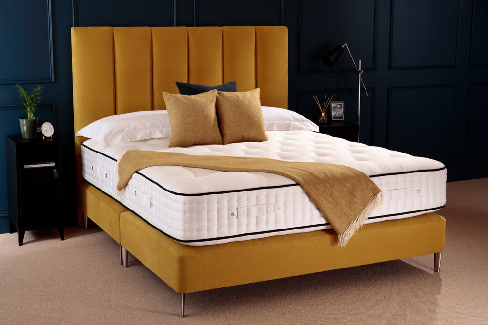 Yellow bed frame with white mattress and brown pillows against a dark blue wall.