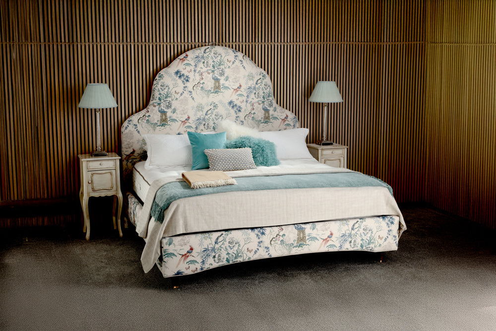 Decorative bed with floral headboard and bedding in a bedroom setting.