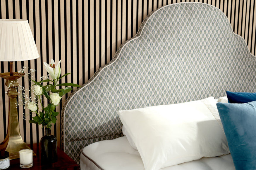 Decorative headboard with pillows and a lamp against striped wallpaper