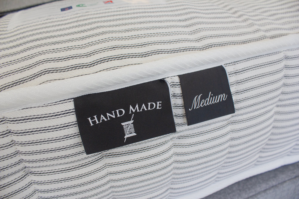 Close-up of a mattress with a 'Hand Made Medium' label on a striped fabric background.